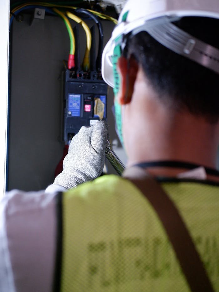 services-02 An electrician using gloves to safely work on a circuit breaker box indoors.