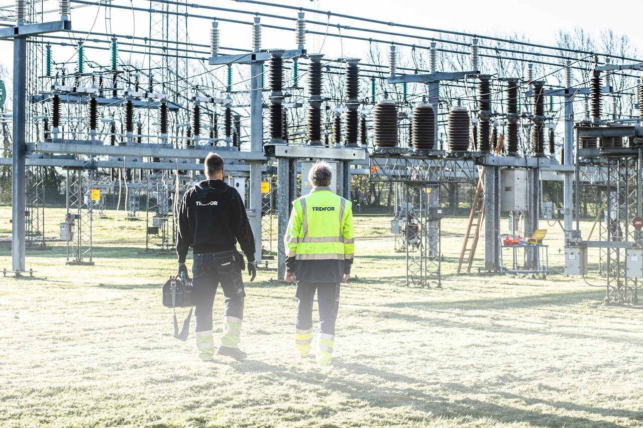 why-choose-us Two workers inspect an outdoor electrical substation, emphasizing safety and maintenance.