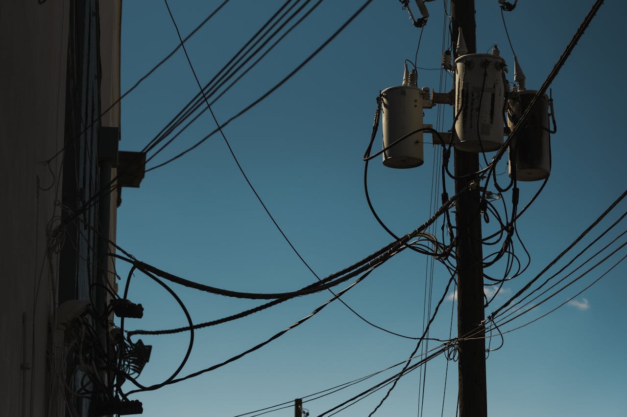 hero-img-02 Low angle view of power lines and transformers against a clear blue sky, depicting modern electricity infrastructure.