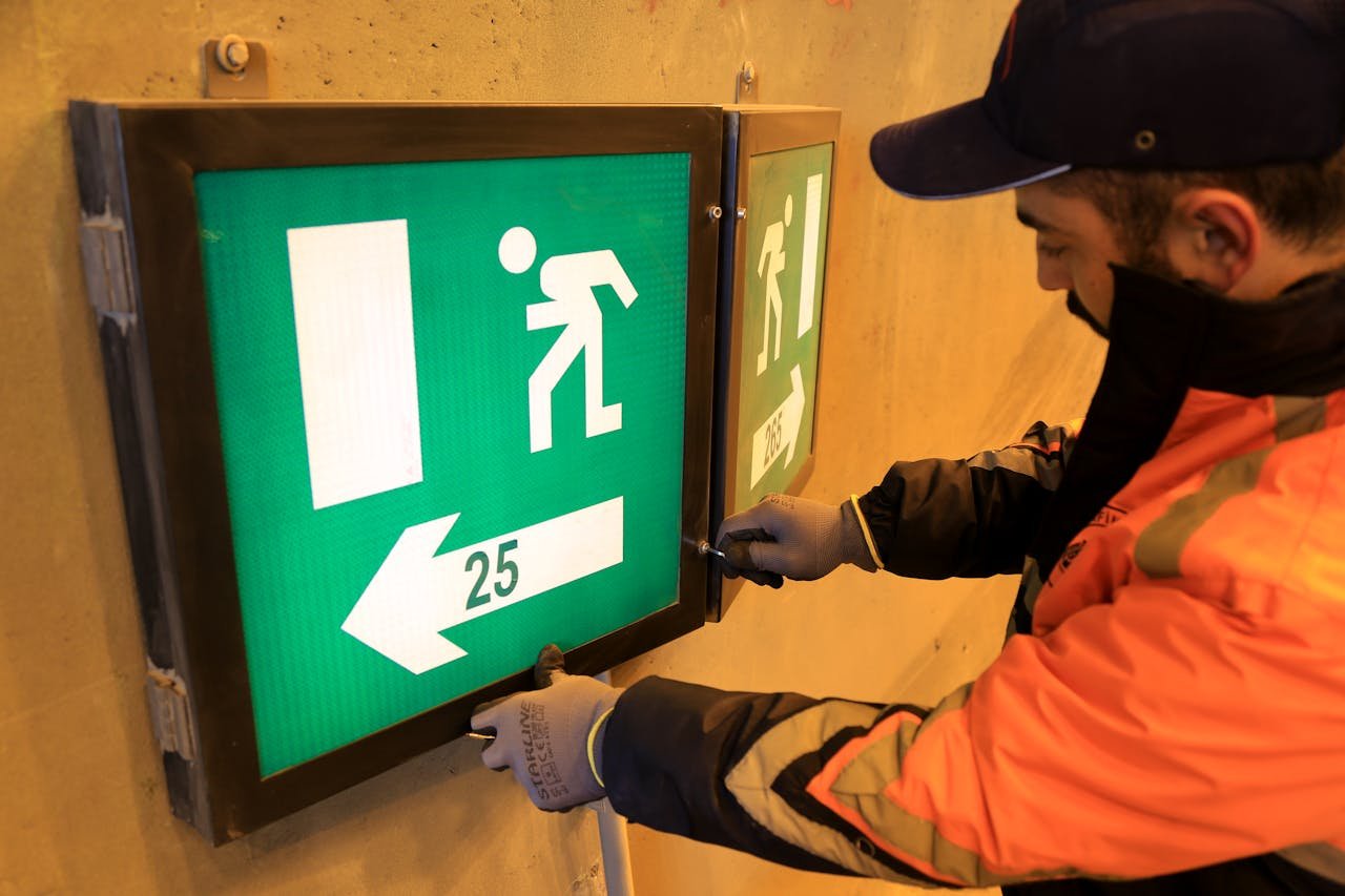 gallery-3 A technician in an orange jacket adjusts an emergency exit sign with directional arrow in a tunnel.