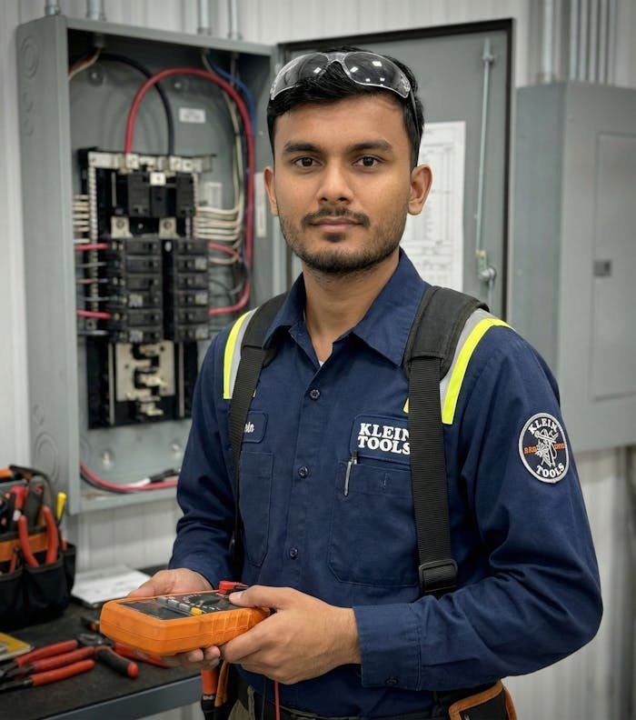 services-03 Electrician in safety gear inspecting circuit breakers with a meter.