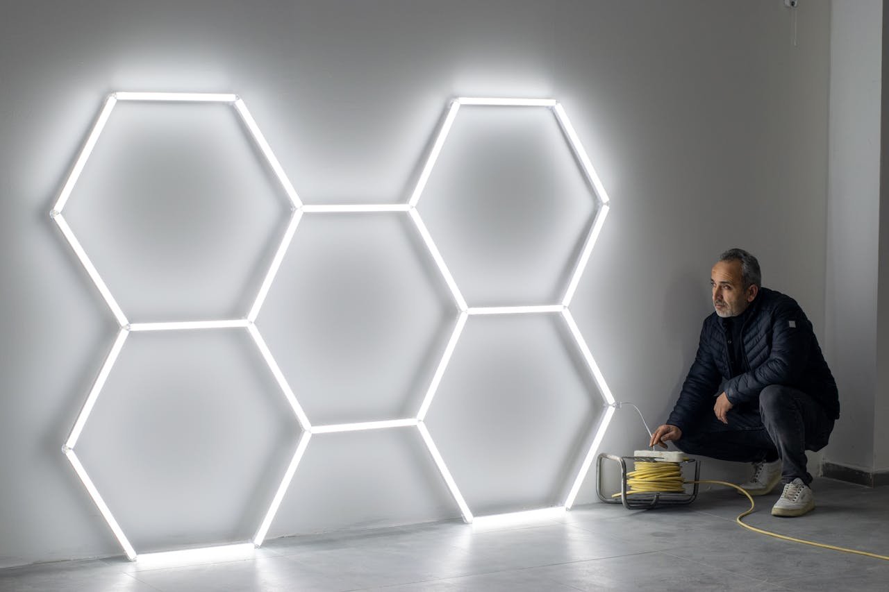 gallery-2 A man installing hexagonal LED light fixtures on a wall, indoors.